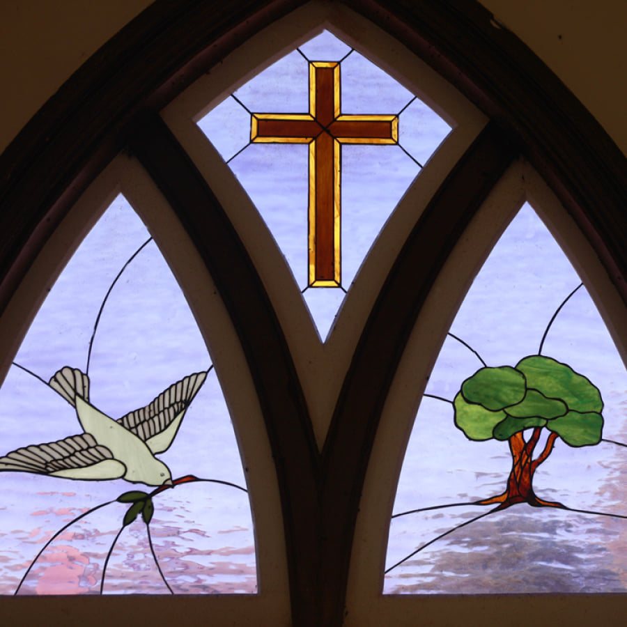 Stained glass church window featuring a dove, cross, and tree of life